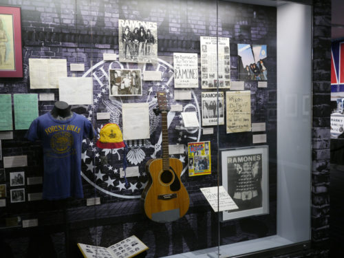 Ramones Forest Hills display featuring an acoustic guitar, clothing, photographs, and handwritten materials
