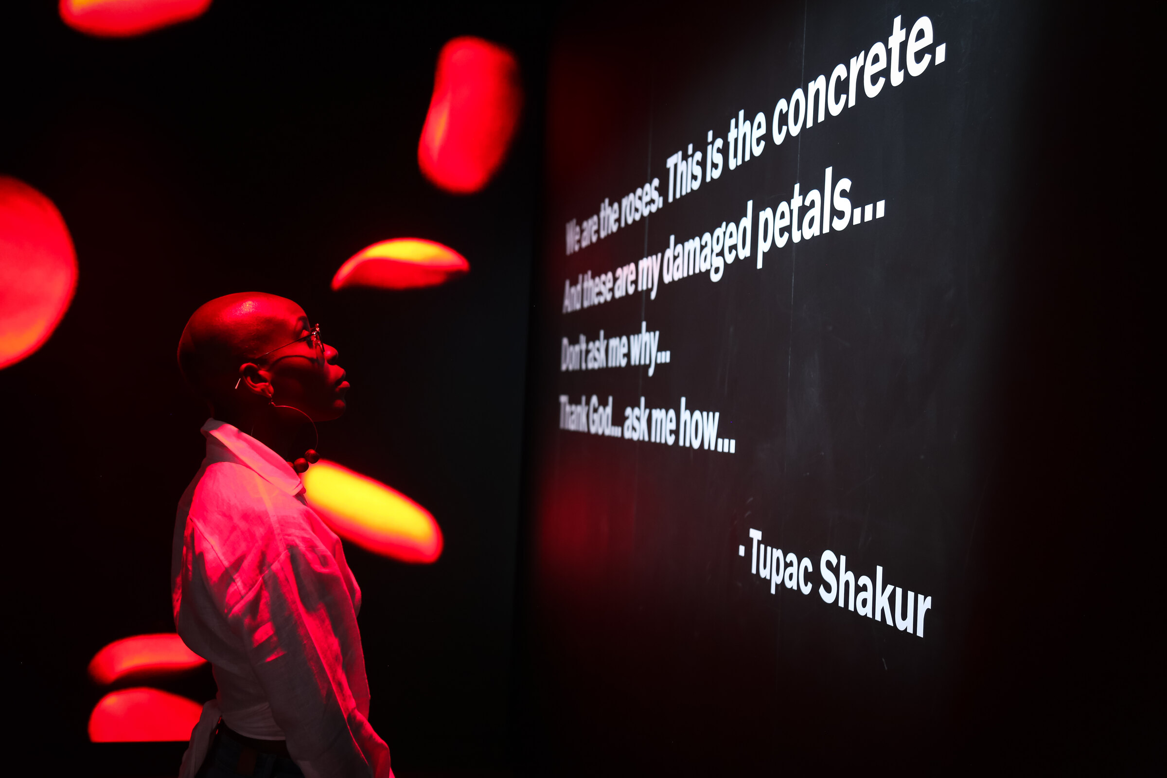 Nwaka Onwusa looking up at Tupac Shakur&rsquo;s rose petal projection in the exhibition